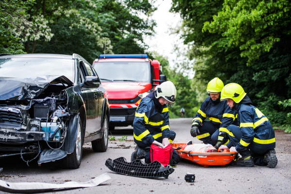 Firefighters helping a young woman after a car accident. A female driver in a plastic stretcher on the countryside road.