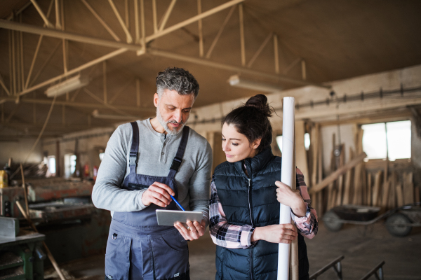 Portrait of a man and woman workers in the carpentry workshop, looking at tablet.