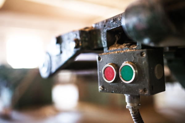 Machine control panel with red and green buttons in carpentry workshop.