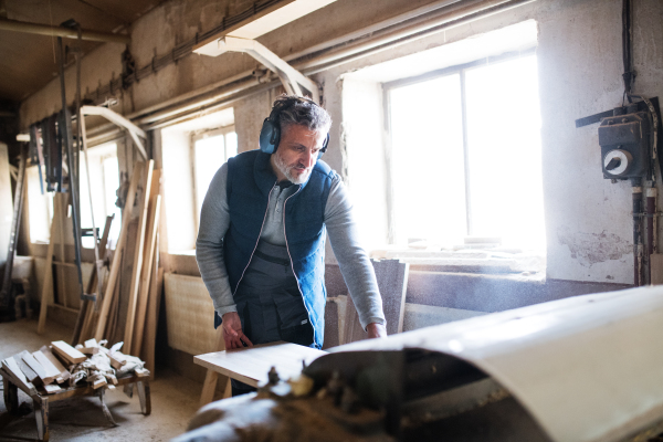 A mature man worker in the carpentry workshop, working with wood.