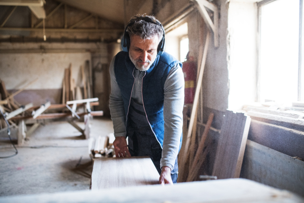 A mature man worker in the carpentry workshop, working with wood.