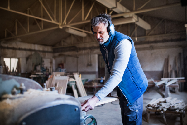 A mature man worker in the carpentry workshop, working with wood.