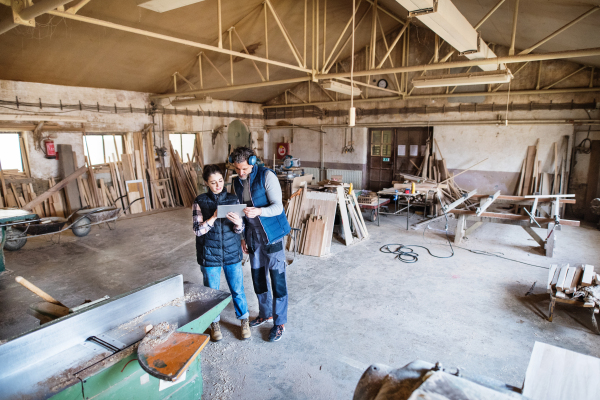 Portrait of a man and woman workers in the carpentry workshop, looking at tablet. Top view.