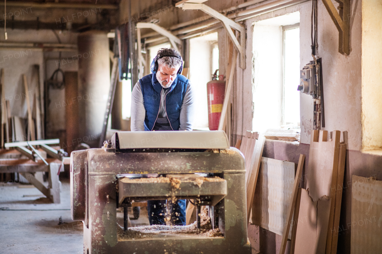 A mature man worker in the carpentry workshop, working with wood.