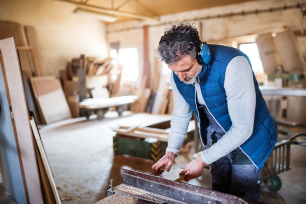 A mature man worker in the carpentry workshop, working with wood.