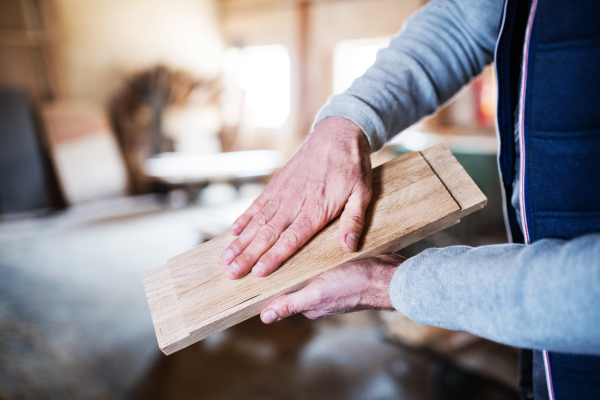 Hands of an unrecognizable man worker working in the carpentry workshop, holding a piece of wood.