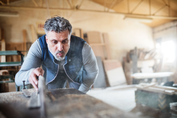 A mature man worker in the carpentry workshop, working with wood.