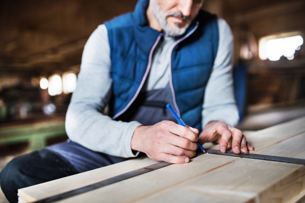 An unrecognizable mature man worker in the carpentry workshop, working with wood.