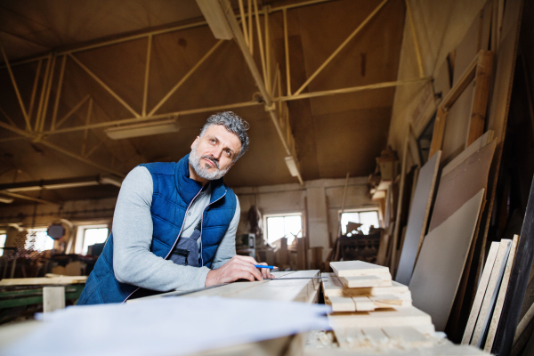 A mature man worker in the carpentry workshop, working with wood.