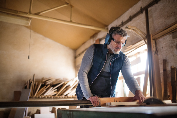 A mature man worker in the carpentry workshop, working with wood.