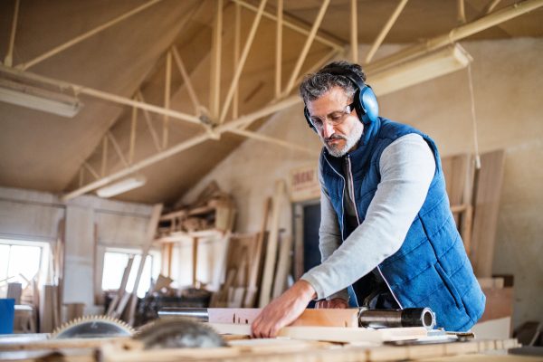 A mature man worker in the carpentry workshop, working with wood.