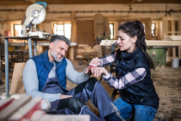 An injured man and woman workers after an accident in the carpentry workshop. A woman helping her colleague.