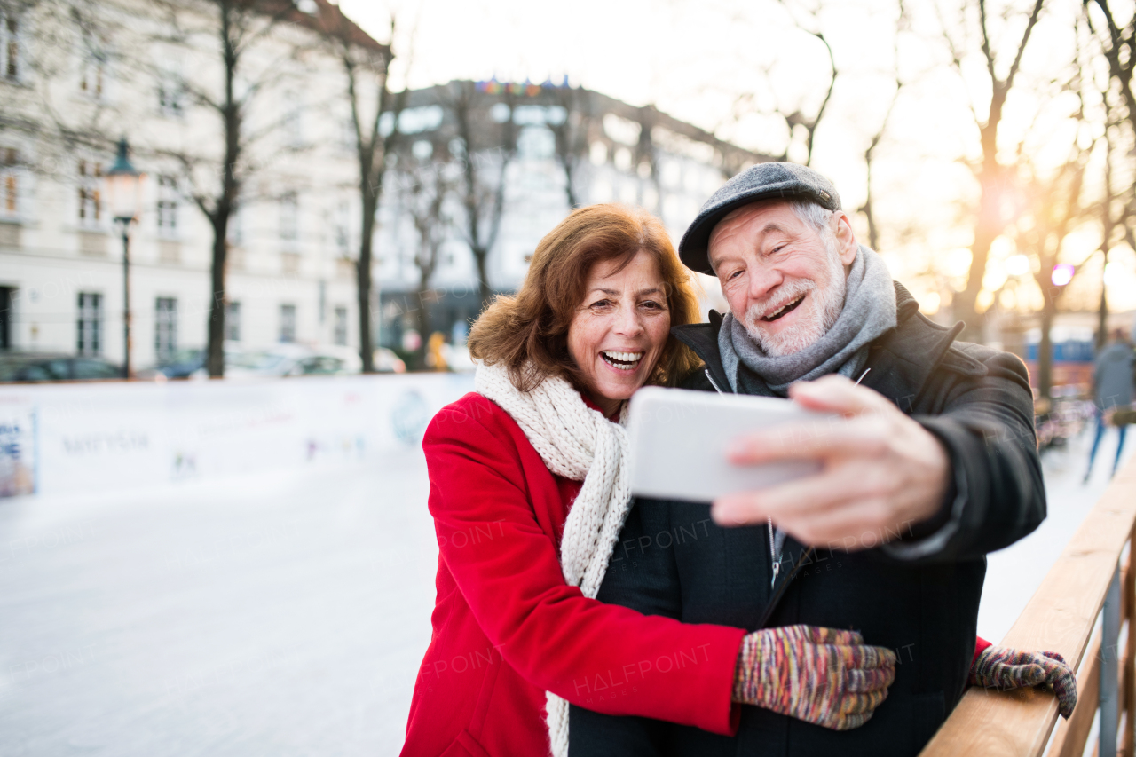 Happy senior couple with smartphone on a walk in a city in winter. A man and woman taking a selfie.