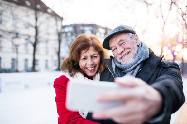 Happy senior couple with smartphone on a walk in a city in winter. A man and woman taking a selfie.