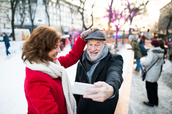 Happy senior couple with smartphone on a walk in a city in winter. A man and woman taking a selfie.