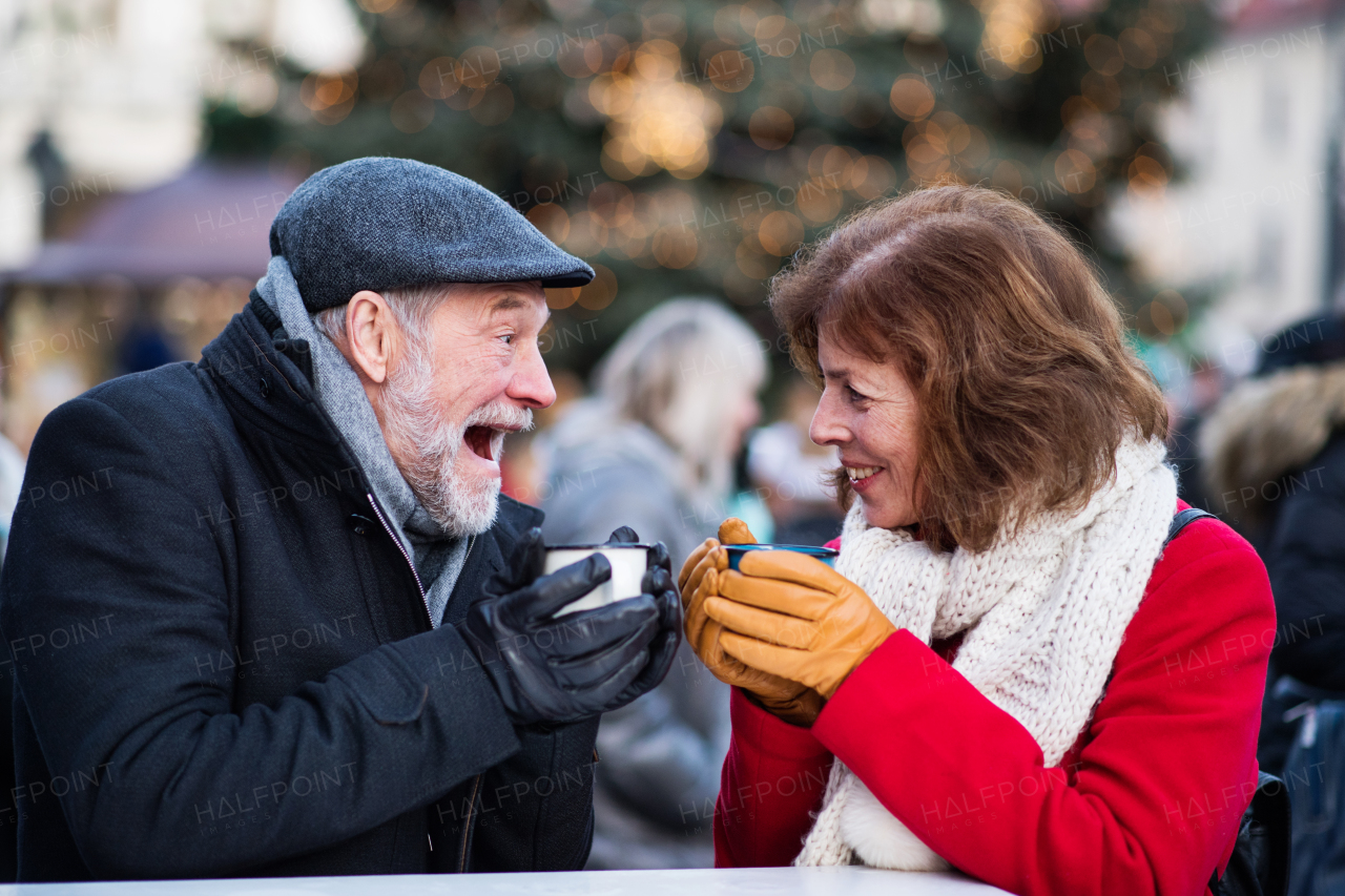 Happy senior couple on an outdoor Christmas market, drinking tea or coffee. Winter time.