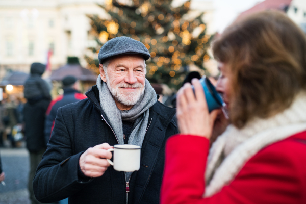 Happy senior couple on an outdoor Christmas market, drinking tea or coffee. Winter time.