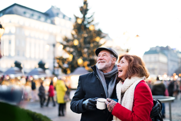 Happy senior couple on an outdoor Christmas market, holding enameled cups. Winter time.