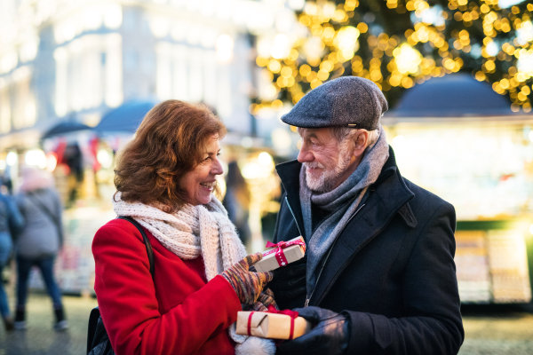 Happy senior couple on an outdoor Christmas market, exchanging presents. Winter time.