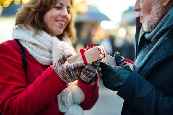 Happy senior couple on an outdoor Christmas market, exchanging presents. Winter time.