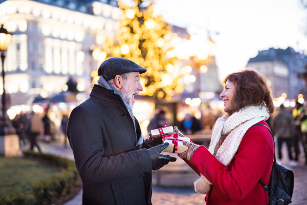 Happy senior couple on an outdoor Christmas market, exchanging presents. Winter time.