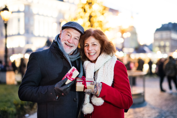 Happy senior couple on an outdoor Christmas market, holding wrapped presents. Winter time.