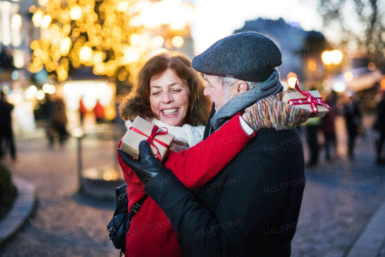 Happy senior couple on an outdoor Christmas market, exchanging presents. Winter time.