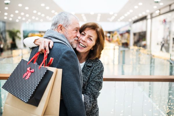 Happy senior couple with paper bags in shopping center looking at each other, hugging and kissing.