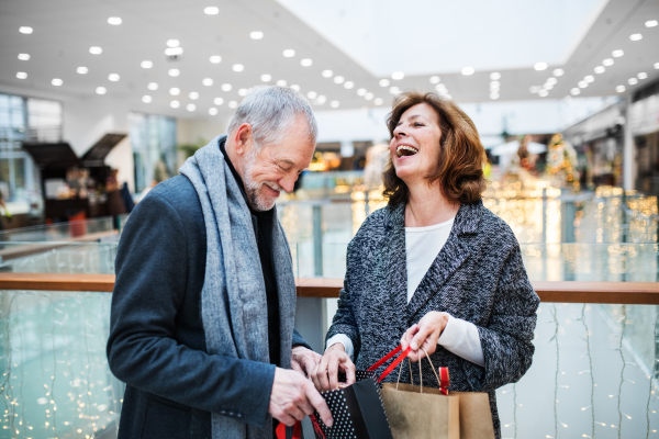 A senior couple with paper bags in shopping center at Christmas time, laughing.