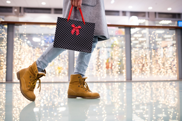 Unrecognizable senior woman with gift paper bag doing Christmas shopping. Shopping center at Christmas time.