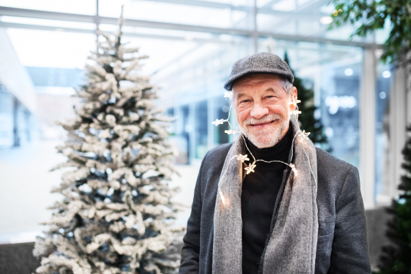 Portrait of senior man standing in shopping center at Christmas time, chain of light around head.