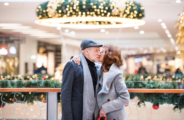 A happy senior couple standing in shopping center in the evening, kissing.