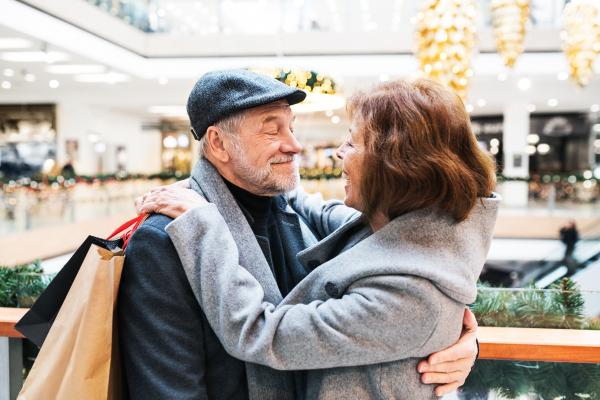 Happy senior couple with paper bags in shopping center looking at each other, hugging.