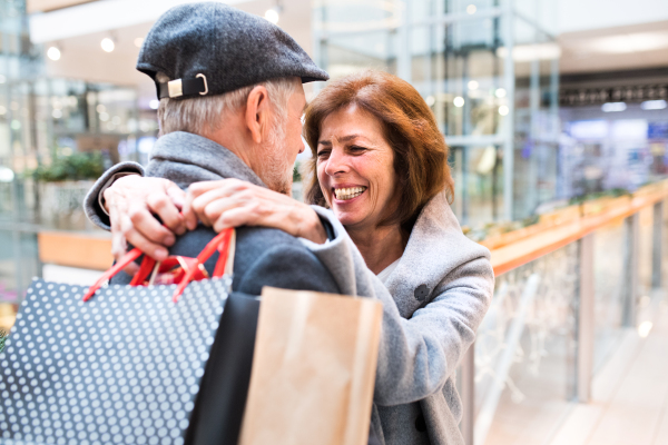 Senior couple doing Christmas shopping, hugging. Shopping center at Christmas time.