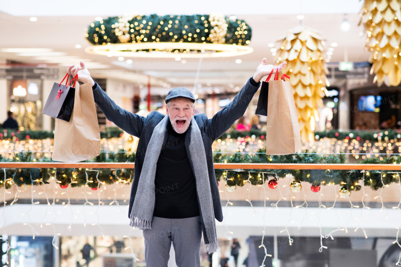 Senior man doing Christmas shopping, having fun. Shopping center at Christmas time.