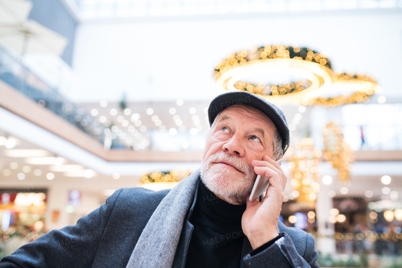 Senior man with smartphone doing Christmas shopping. A man making a phone call. Shopping center at Christmas time.