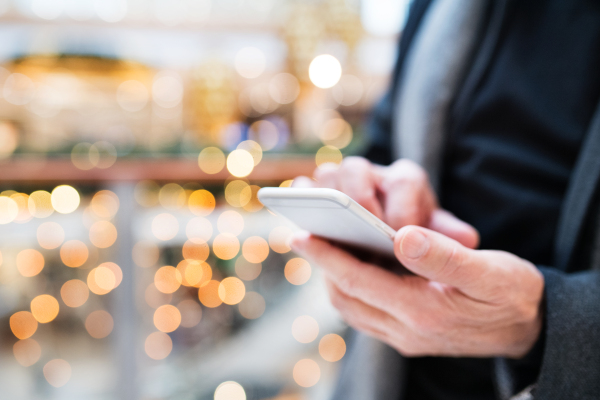 Senior man with smartphone doing Christmas shopping. Unrecognizable man text messaging. Shopping center at Christmas time. Close up.