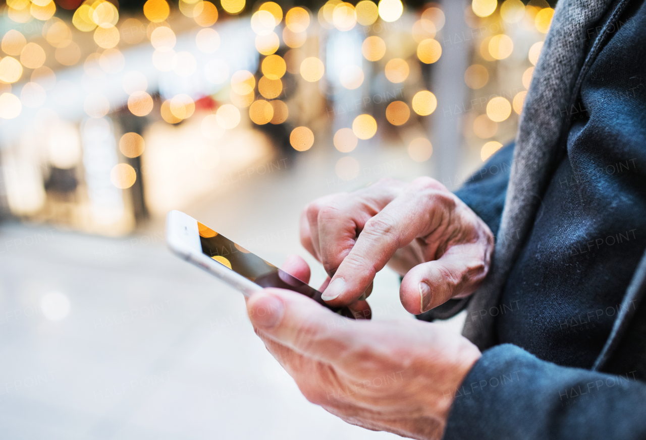 Unrecognizable senior man with smartphone in shopping centre at Christmas time, text messaging. Close up.