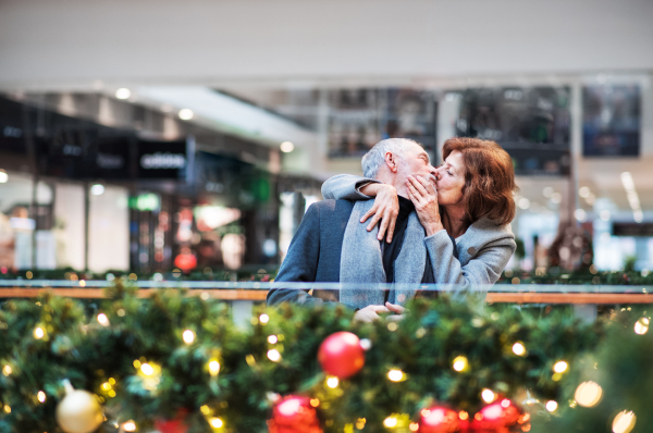 A portrait of happy senior couple in shopping center at Christmas time, kissing.