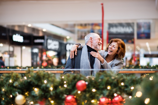 Senior couple doing Christmas shopping, having fun. Shopping center at Christmas time.