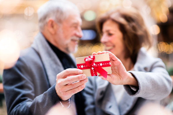 Senior couple doing Christmas shopping. A man and woman holding a present. Shopping center at Christmas time.