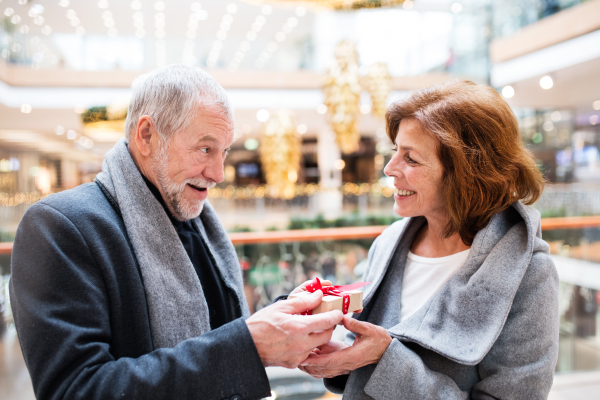 Senior couple doing Christmas shopping. A man giving a present to a woman. Shopping center at Christmas time.