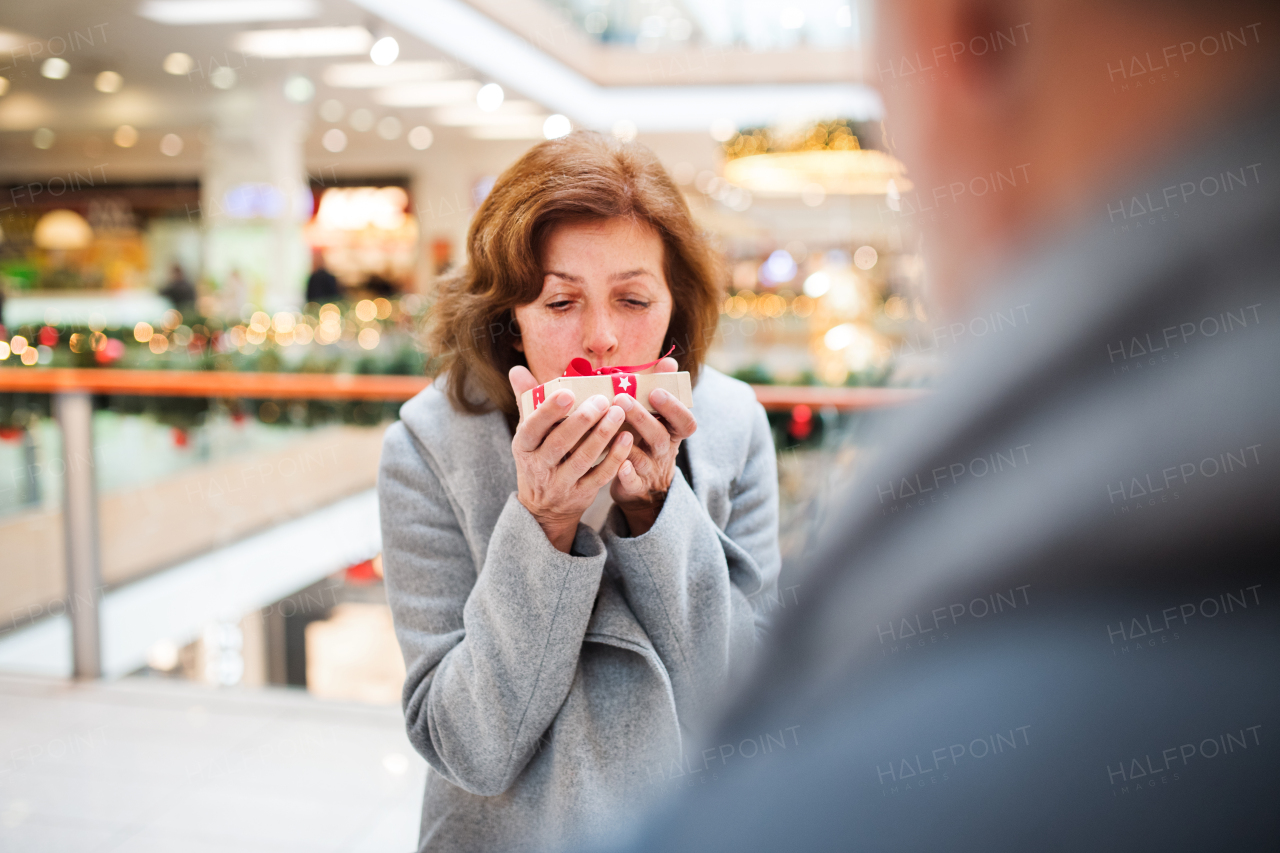 Senior couple doing Christmas shopping. An unrecognizable man giving a present to a woman. Shopping center at Christmas time.