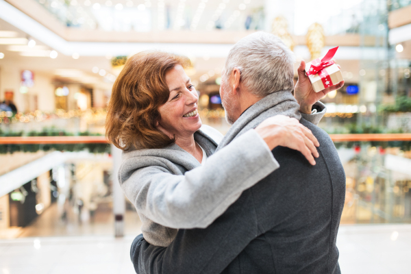 Senior couple doing Christmas shopping. An unrecognizable man giving a present to a woman. Shopping center at Christmas time.