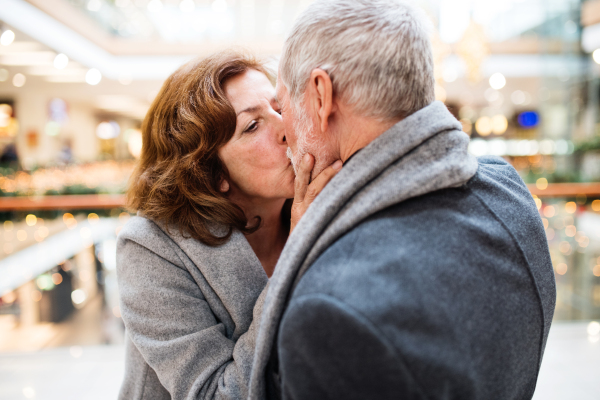 Senior couple doing Christmas shopping. Man and woman kissing. Shopping center at Christmas time.