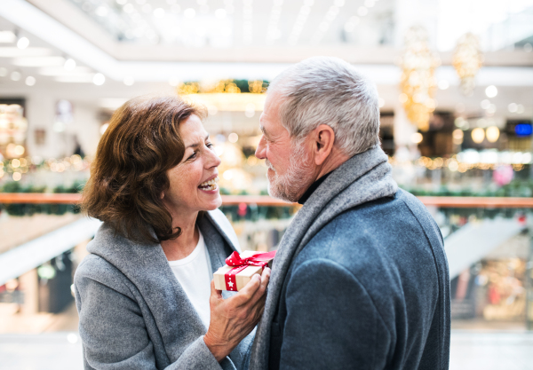 A senior man giving a present to a happy woman at shopping center at Christmas time.