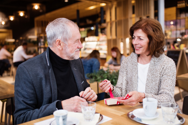 Senior couple in a cafe. A woman opening a present. Shopping center at Christmas time.