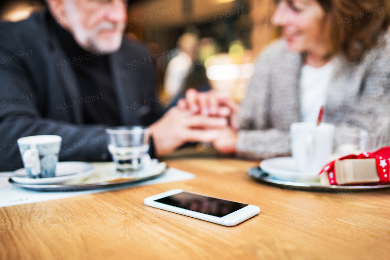 Senior couple with smartphone in a cafe, holding hands. Shopping center at Christmas time.