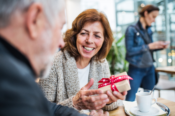 Senior couple in a cafe. A woman holding a present. Shopping center at Christmas time.