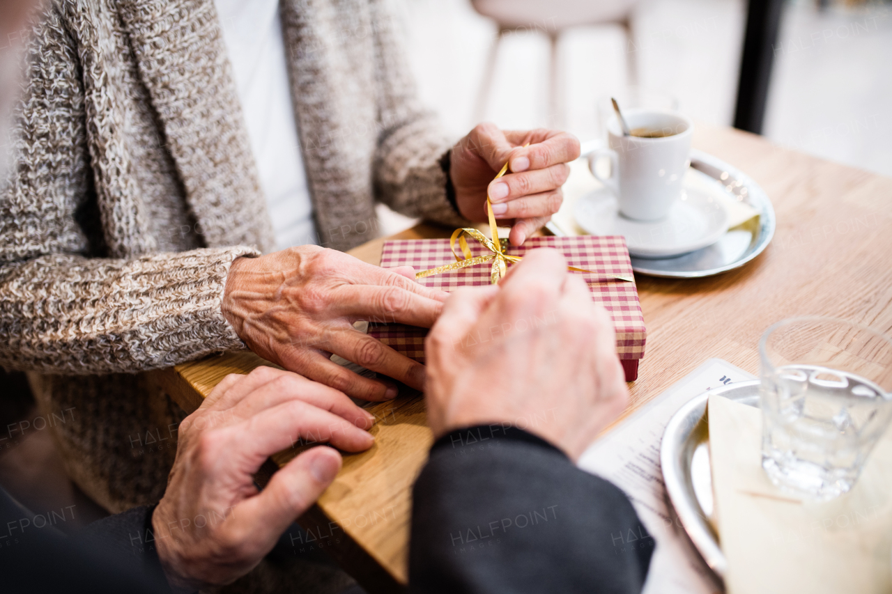 Unrecognizable senior couple in a cafe. A woman opening a present.